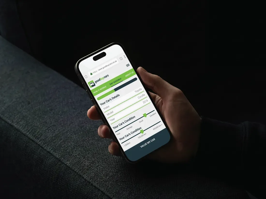 Hand holding a phone showing the Good Buy Cars valuation form with green progress steps for your car’s details and condition.