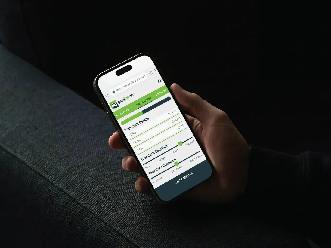 Hand holding a phone showing the Good Buy Cars valuation form with green progress steps for your car’s details and condition.