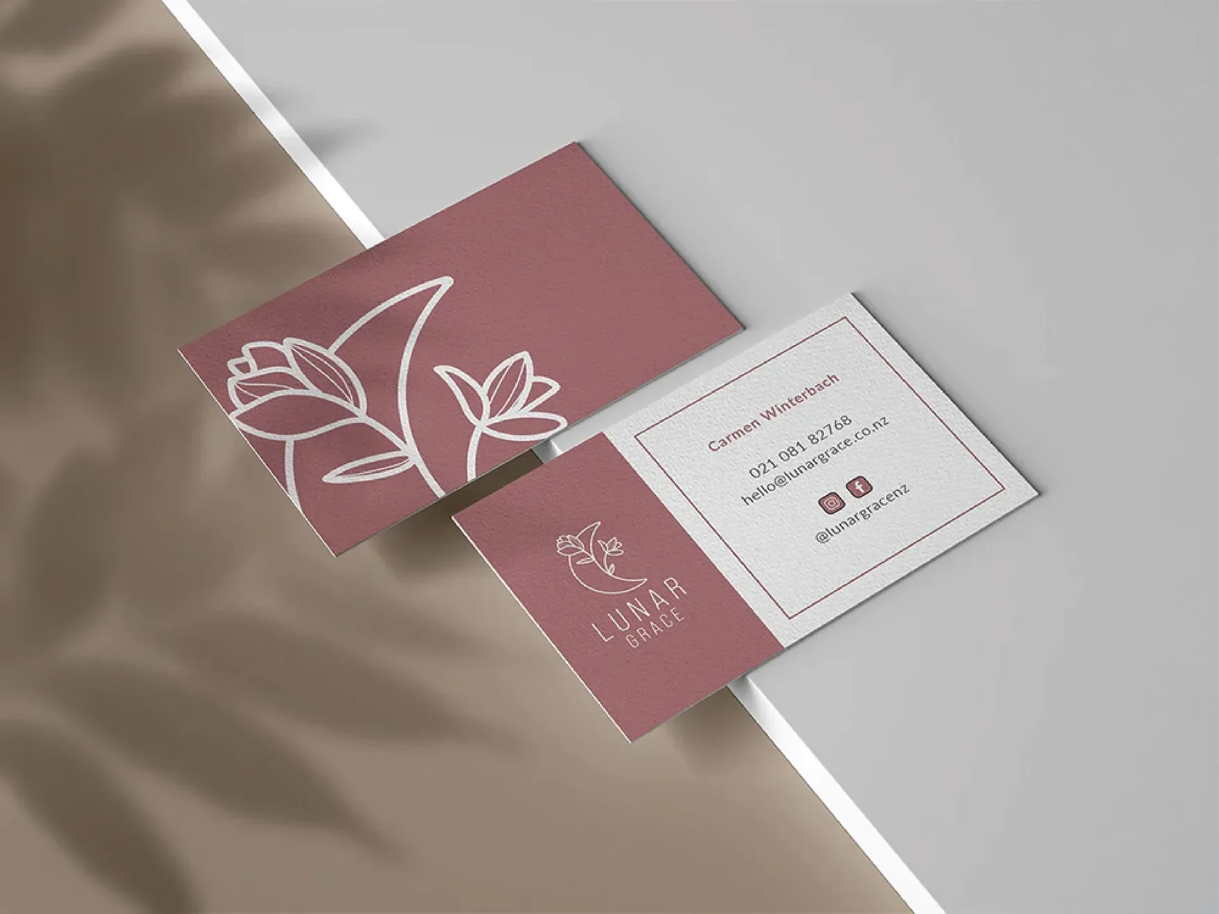 Mauve and white Lunar Grace business cards on a grey surface.