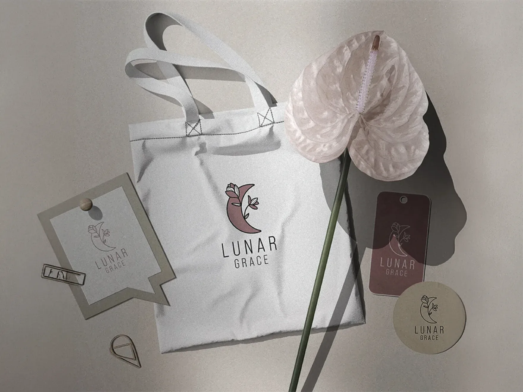 White Lunar Grace tote bag and swing tags with the line mark, styled with a pale anthurium flower.